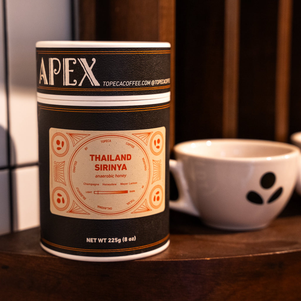 Apex coffee canister on a wooden surface with cups in the background